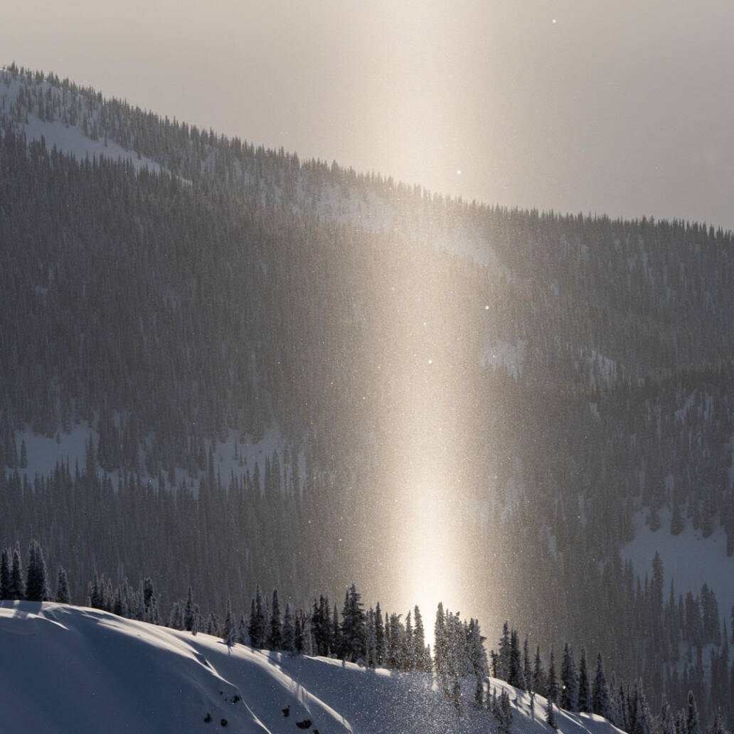 Snow-covered mountain with a radiant stream of sunlight in the foreground, capturing the breathtaking vistas at White Grizzly Cat Skiing in BC, Canada.