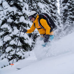 Skier in an orange jacket, donning a smile, gracefully descending downhill, reflecting the exhilarating adventures at White Grizzly Cat Skiing in BC, Canada.