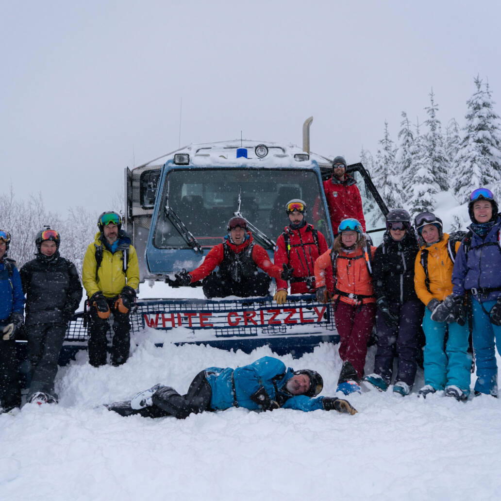 Smiling group of skiers donning vibrant jackets, posed in front of a snowcat, epitomizing the camaraderie and adventure at White Grizzly Cat Skiing in BC, Canada.