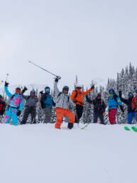 Group of skiers in vibrant jackets striking a triumphant pose with arms raised at White Grizzly Cat Skiing.