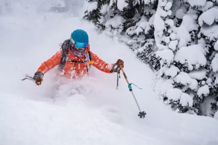 Skier in vibrant orange attire and a teal helmet, deeply engrossed in carving turns amidst the powder, exemplifying the top-tier cat skiing experiences at White Grizzly in BC.