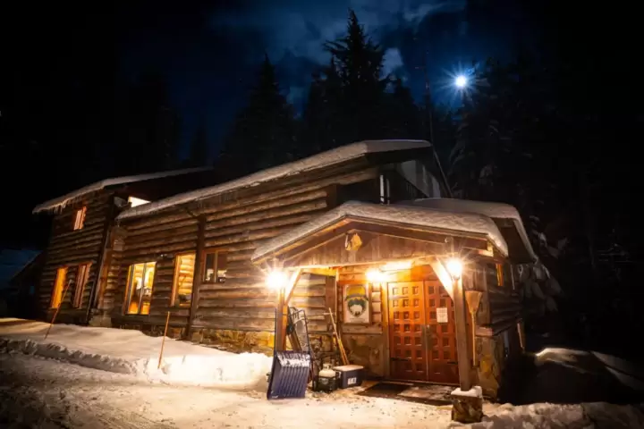 The distinctively crafted timber-adorned White Grizzly cat skiing lodge in BC, Canada, nestled amidst the alpine forest with a breathtaking mountain view.