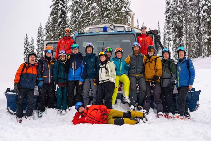 Guides and guests jubilantly gathered in front of a snow cat, celebrating a remarkable day at White Grizzly cat skiing in BC, Canada.