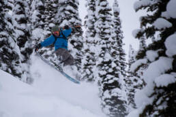 Lodge guest skier performing a tail grab amidst the evergreen trees at White Grizzly cat skiing in BC, Canada.