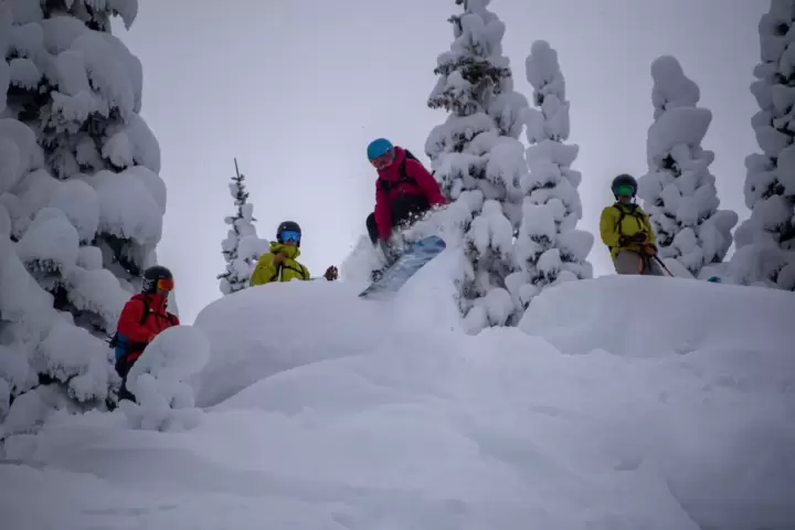 Snowboarder smoothly hopping off a 5-foot ledge in the BC backcountry during a day with White Grizzly cat skiing.